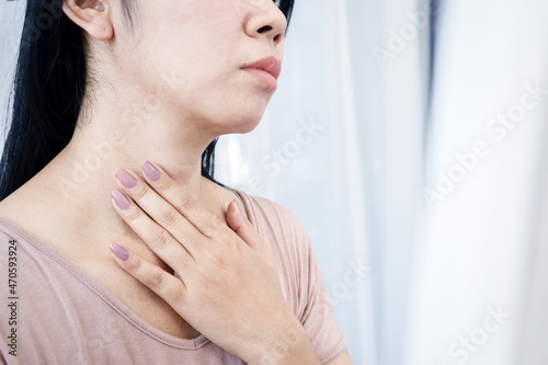 Asian woman having sore throat, hand touching neck feeling pain from inflammation photo