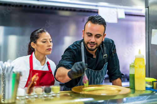 Chef teaching plating to student in restaurant kitchen