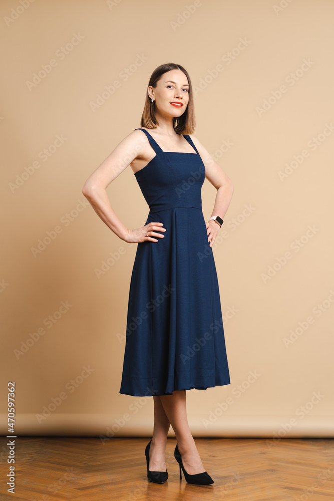 Fototapeta premium Beautiful woman pretty face bright face care dark blonde hair wear clothes short blue dress on beige background