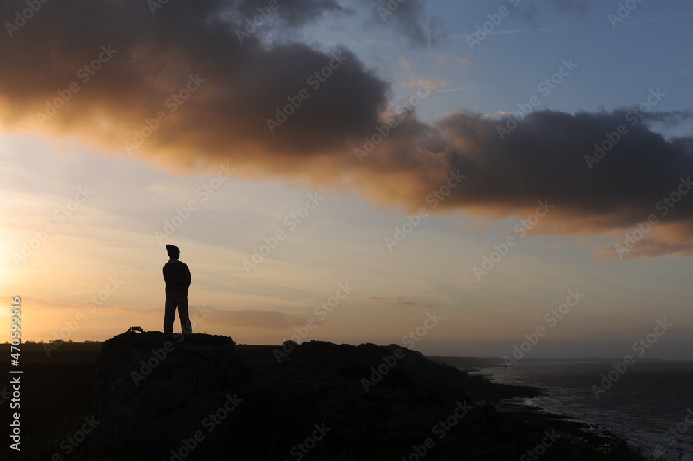 Single man silhouette on a beach at seacoast for outdoor advertisement during sunset at dusk in the evening with clouds and orange sky