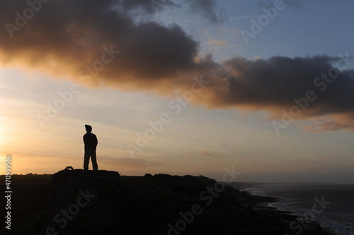 Single man silhouette on a beach at seacoast for outdoor advertisement during sunset at dusk in the evening with clouds and orange sky