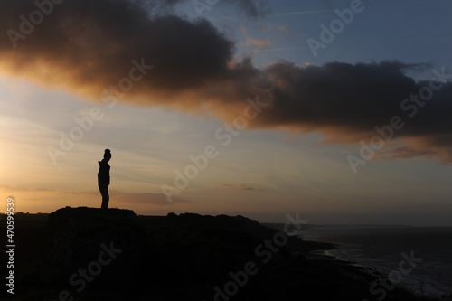 Single man silhouette on a beach at seacoast for outdoor advertisement during sunset at dusk in the evening with clouds and orange sky © piotrmilewski