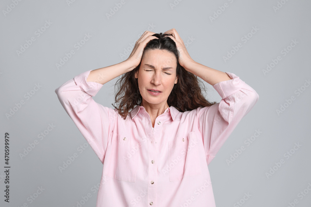 Mature woman suffering from headache on light grey background Mature woman suffering from headache on light grey background
