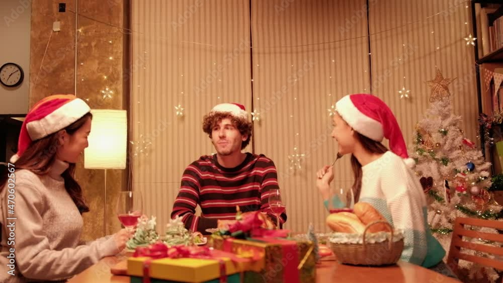 Friends enjoy fun eating diner at table with specials foods, a young woman feeding the man in the home's dining room, decorated with ornaments for Christmas festival and New Year celebration party. Friends enjoy fun eating diner at table with specials foods, a young woman feeding the man in the home's dining room, decorated with ornaments for Christmas festival and New Year celebration party.