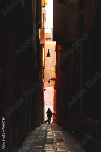 Silhouette d'homme au bout d'une ruelle sombre, en fond le coucher de soleil. photo