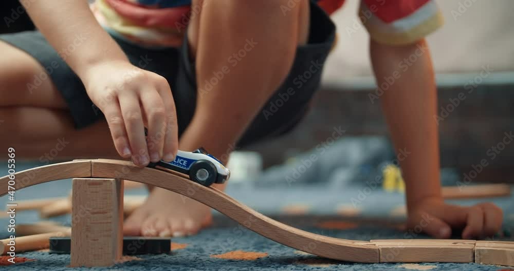 Close up of child boy hands playing with toy police car on wooden railway road in living room at evening in home. Concept of playful carefree childhood with toys