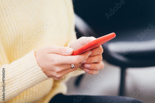 Close-up of woman in pale yellow jumper holding in hands modern smartphone in red case. Opening QR code to show in entrance. Reading news and blogs  social network  watching videos photos  surfing web