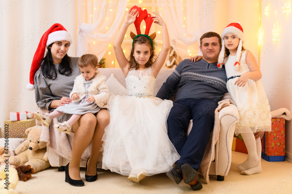 happy big family portrait, celebrating new year or Christmas - parents and children in home interior decorated with holiday lights and gifts, dressed in santa hat