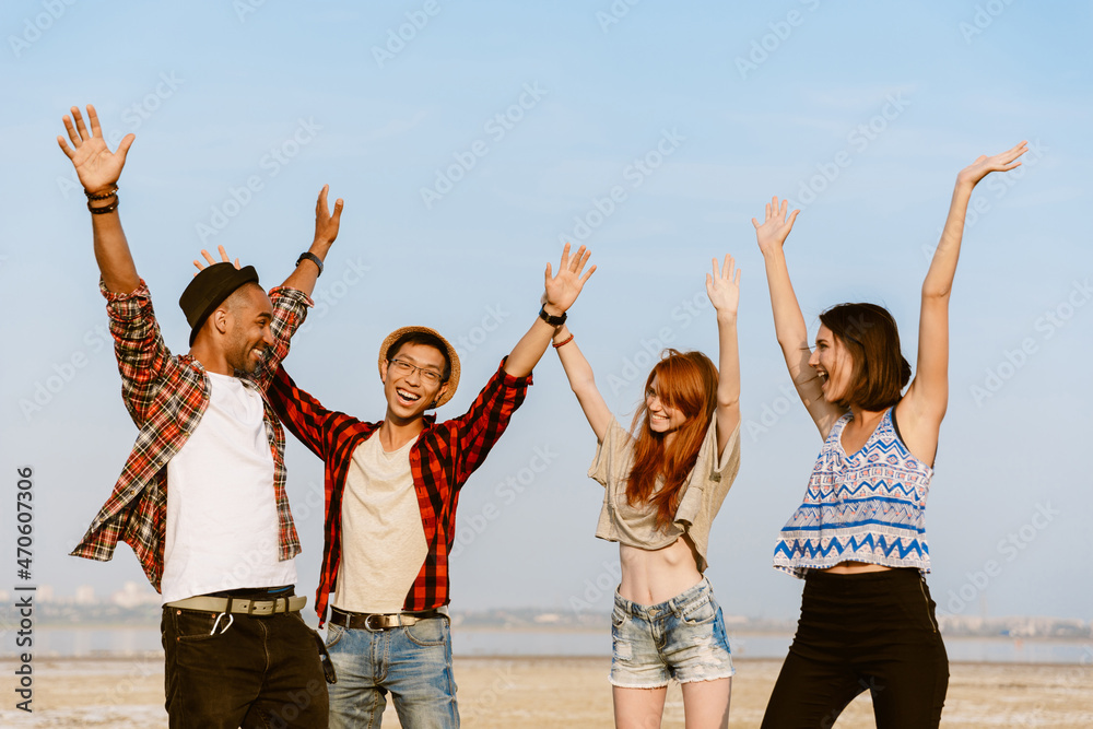 Obraz premium Young multiracial friends laughing while posing with hands up