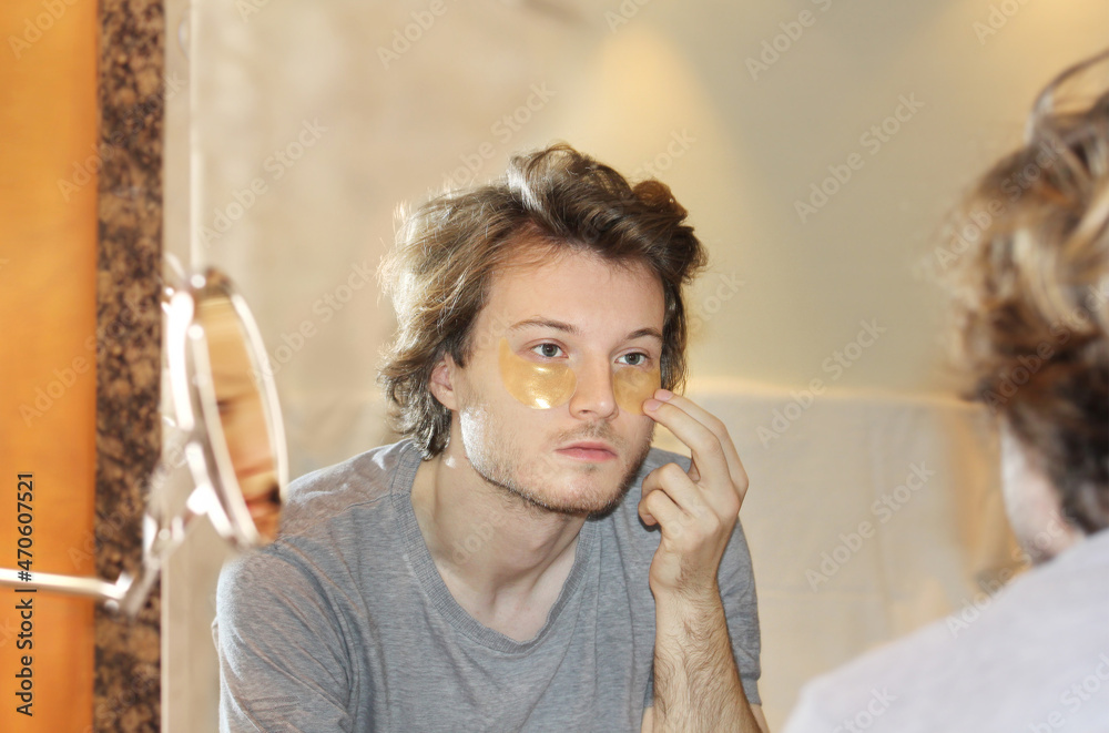 Fototapeta premium Anti-aging eye therapy. young man taking care of his undereye wrinkles applying facial mask. Dark Circles.Eye patches..