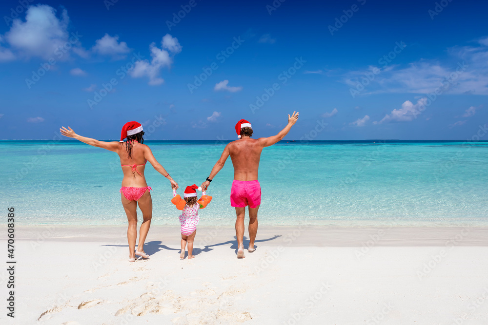 A happy family with santa claus hats runs into the turquoise sea of a tropical paradise beach during their christmas holidays
