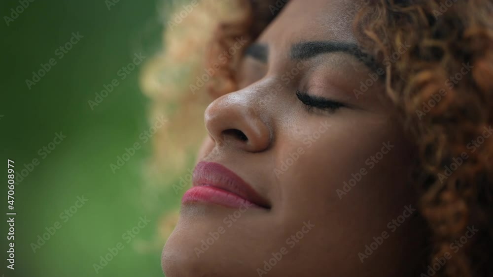 African woman taking a deep breath outside in nature looking up at sky smiling feeling free
