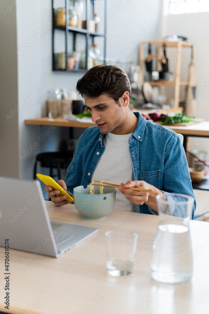 Young man using smart phone while having noodles at home Young man using smart phone while having noodles at home