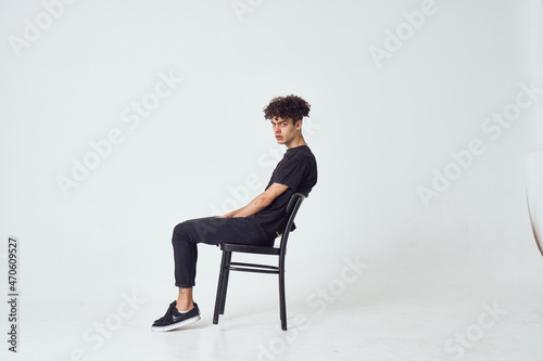 curly guy sitting on a chair posing fashion light background
