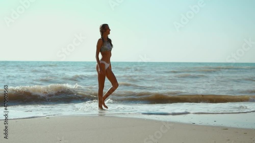 happy carefree slender woman with beautiful fitbody running along seashore of sea with waves after storm, girl jogging and jumping through waves photo