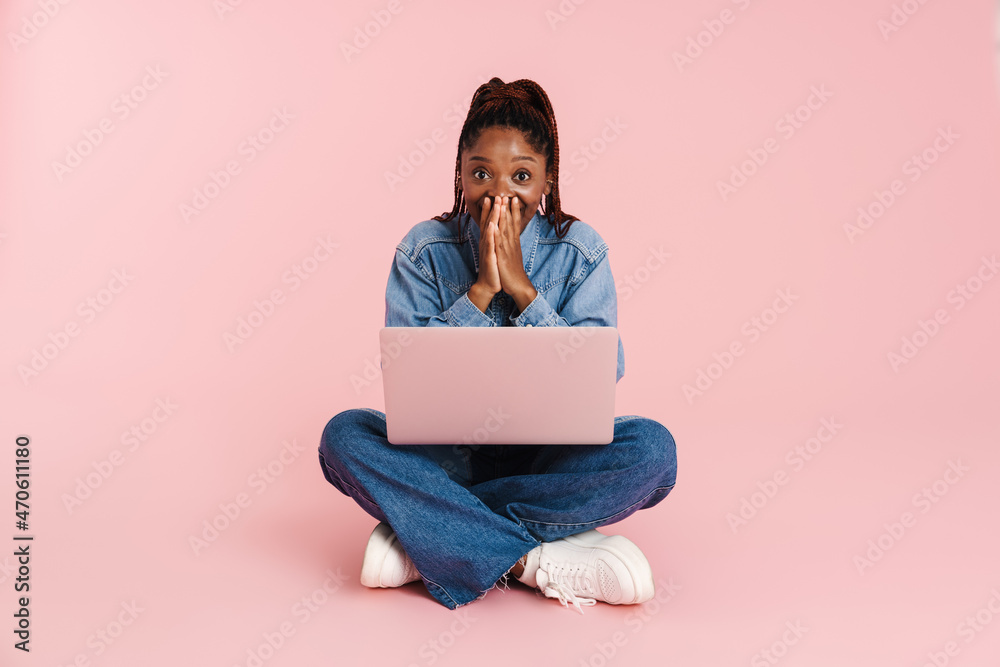 Black woman expressing surprise and using laptop while sitting on floor Black woman expressing surprise and using laptop while sitting on floor