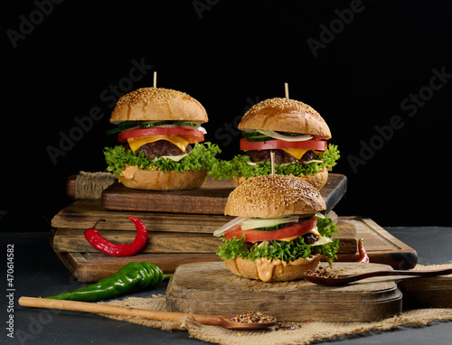 cheeseburger with grilled beef patty, cheddar cheese, tomato and lettuce on a wooden board, black background
