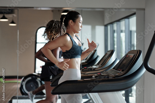 Concentrated young woman jogging on treadmill next to her friend