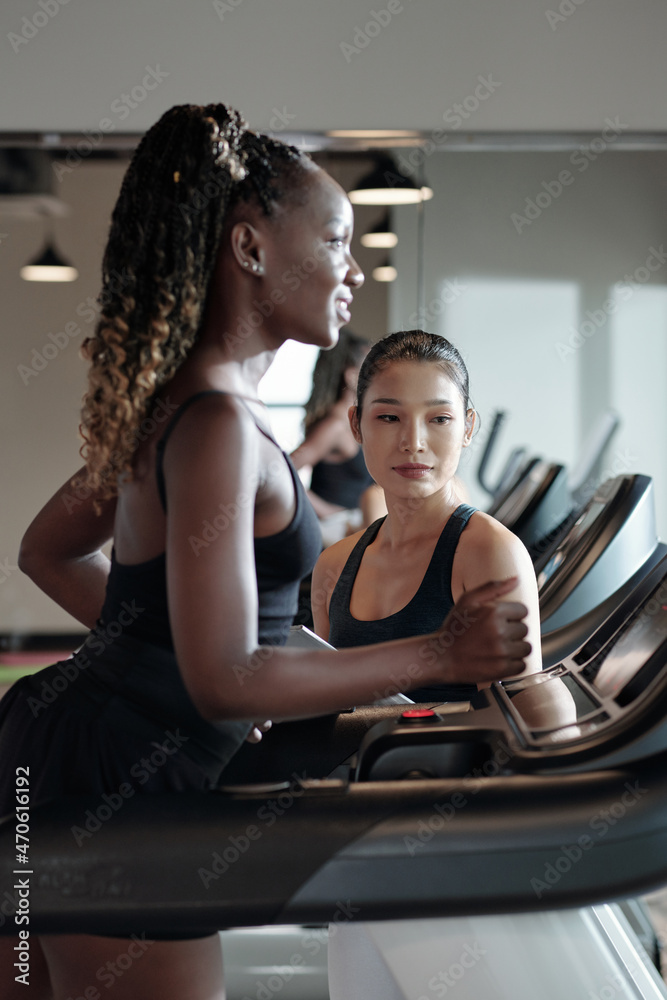 Fitness trainer controlling her female client running on treadmill before working out Fitness trainer controlling her female client running on treadmill before working out