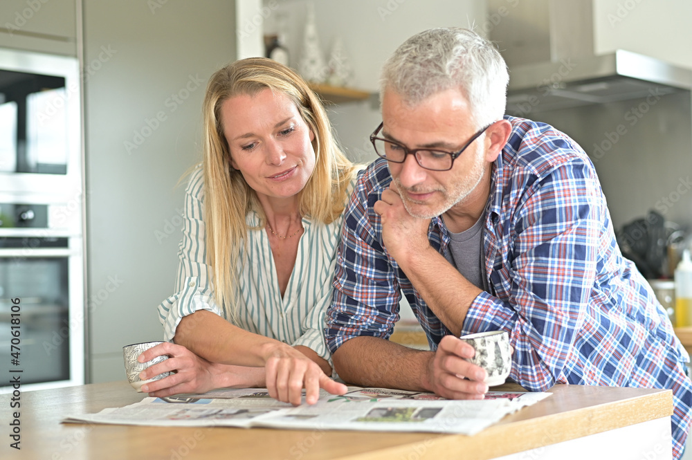 Middle-aged couple in kitchen reading newspaper Middle-aged couple in kitchen reading newspaper