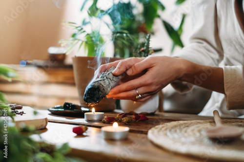 Fotografie Woman hands burning white sage, palo santo before ritual on the table with candles and green plants
