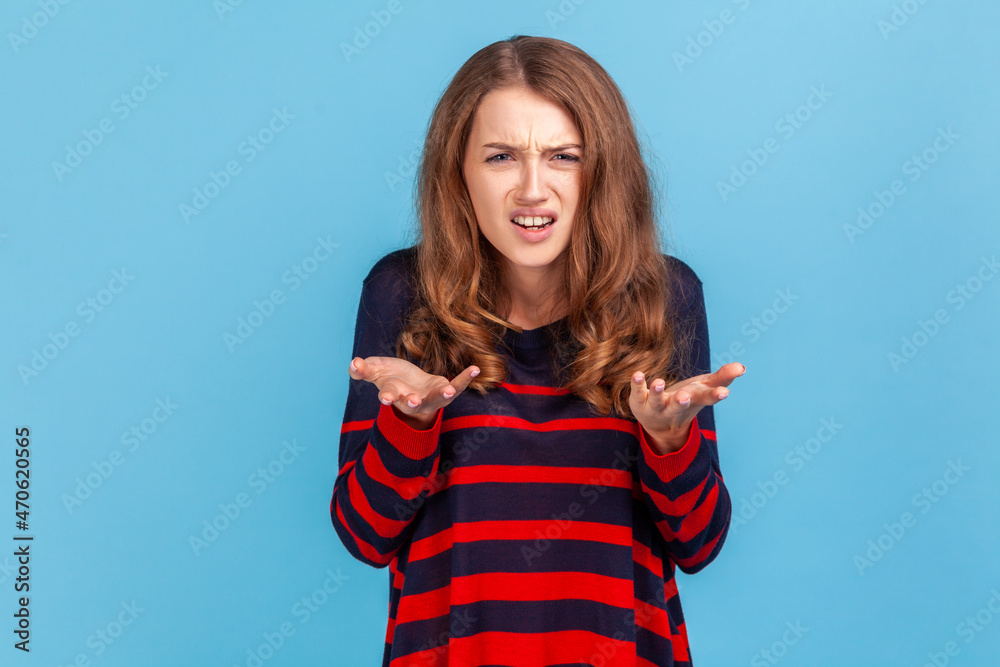 Fototapeta premium What's the problem? Portrait of irritated indignant woman, raising hands in anger and shouting why how, what do you want, quarreling, wearing sweater. Indoor studio shot isolated on blue background.