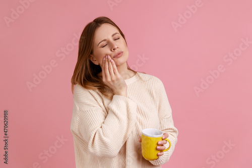 Tableau sur toile Portrait of unhealthy ill blond woman felling toothache after drinking hot or cold beverage, holding cup in hand, wearing white sweater