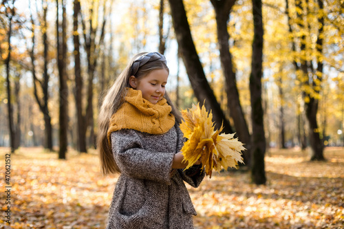 Smiling girl wearing woolen scarf holding bunch of autumn leaves in park