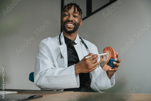 Smiling doctor with digitized pen pointing at anatomical brain model in office photo