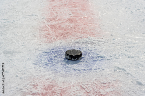 Clean empty ice hockey rink. Skate blade marks and snow crumbs. On surface of ice in center of throw-in circle is old game puck.