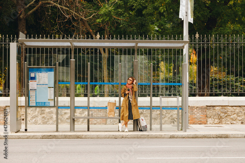 Woman in trench coat waiting at bus stop