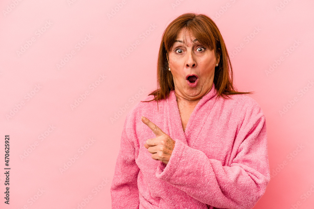 Middle age caucasian woman wearing a bathrobe isolated on pink background pointing to the side