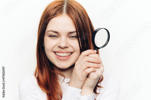 red-haired woman in a white shirt with a magnifying glass in her hands searching