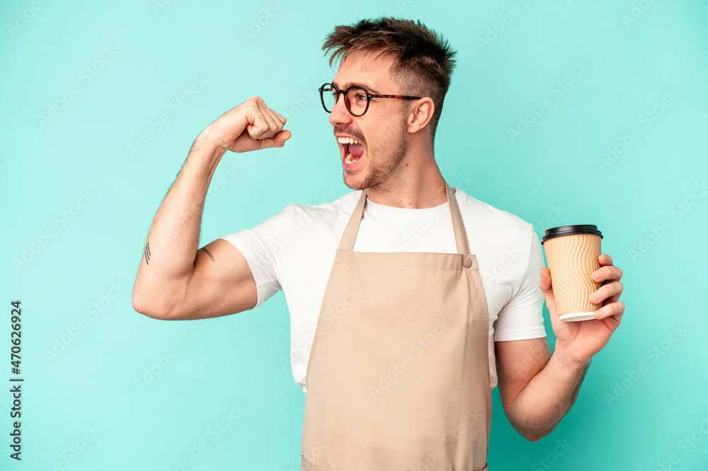Young store clerk man holding a coffee isolated on blue background raising fist after a victory, winner concept. Young store clerk man holding a coffee isolated on blue background raising fist after a victory, winner concept.