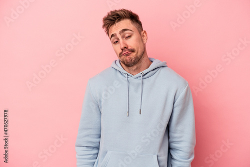 Young caucasian man isolated on pink background shrugs shoulders and open eyes confused.