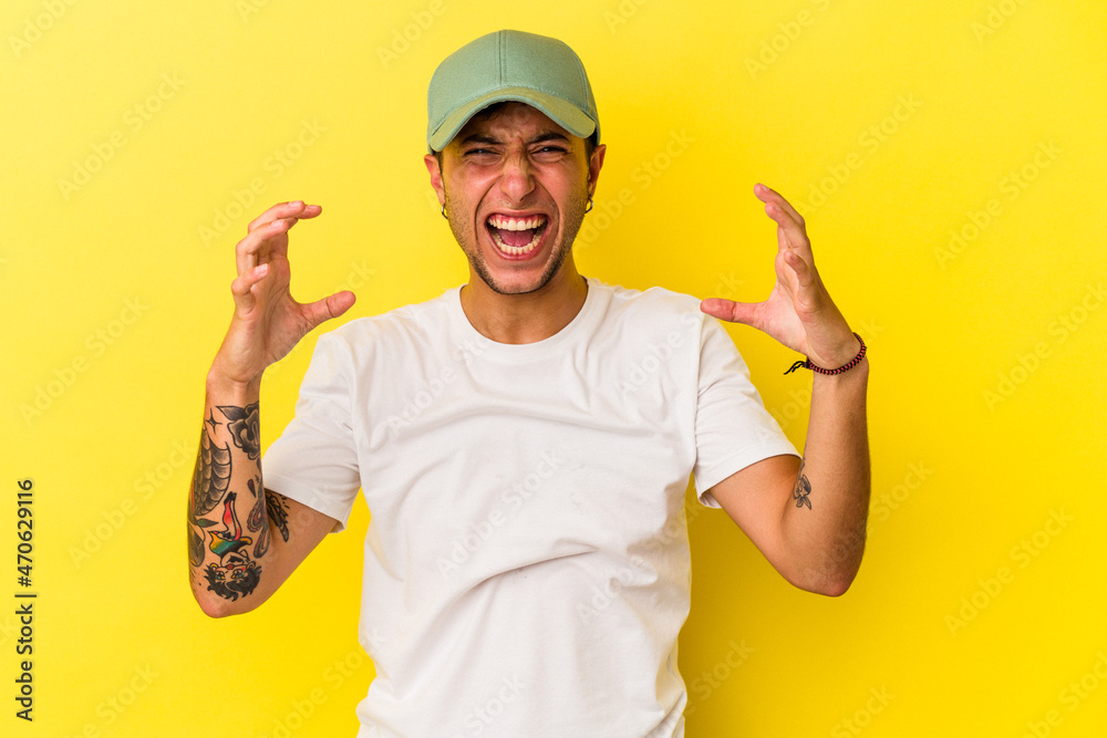Young caucasian man with tattoos isolated on yellow background screaming with rage. Young caucasian man with tattoos isolated on yellow background screaming with rage.