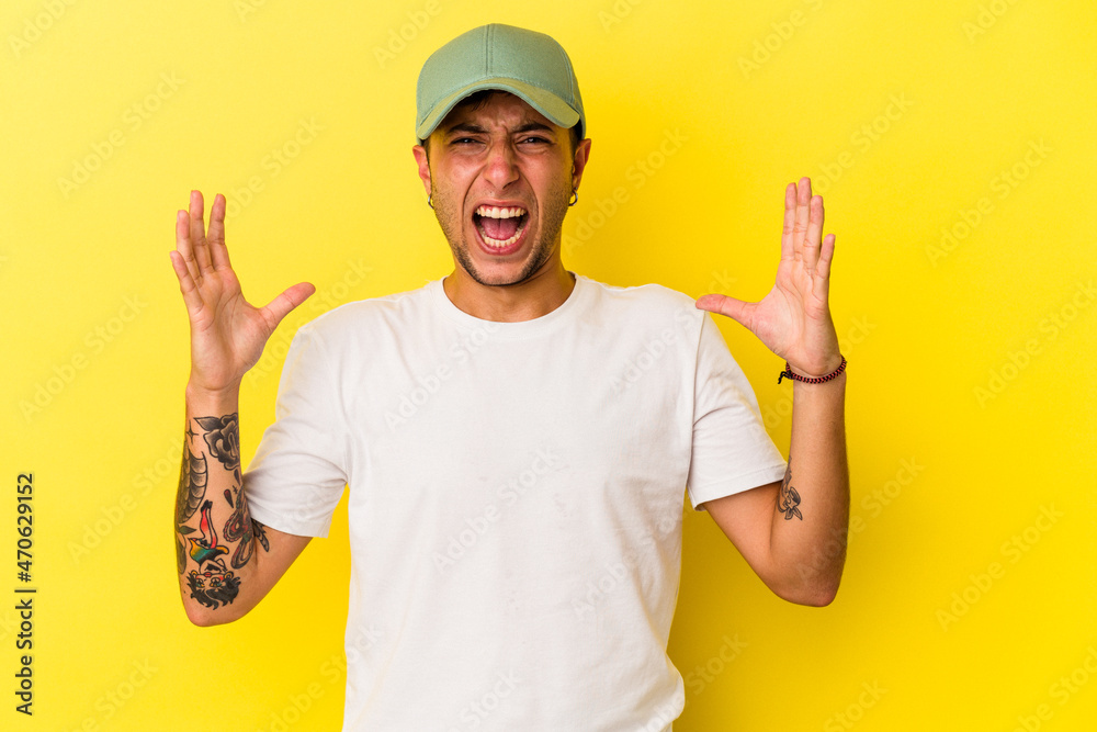 Young caucasian man with tattoos isolated on yellow background  screaming to the sky, looking up, frustrated.