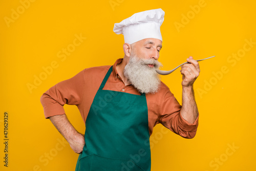 Portrait of attractive dreamy grey-haired man chef tasting lunch fast food cafe service isolated over vivid yellow color background
