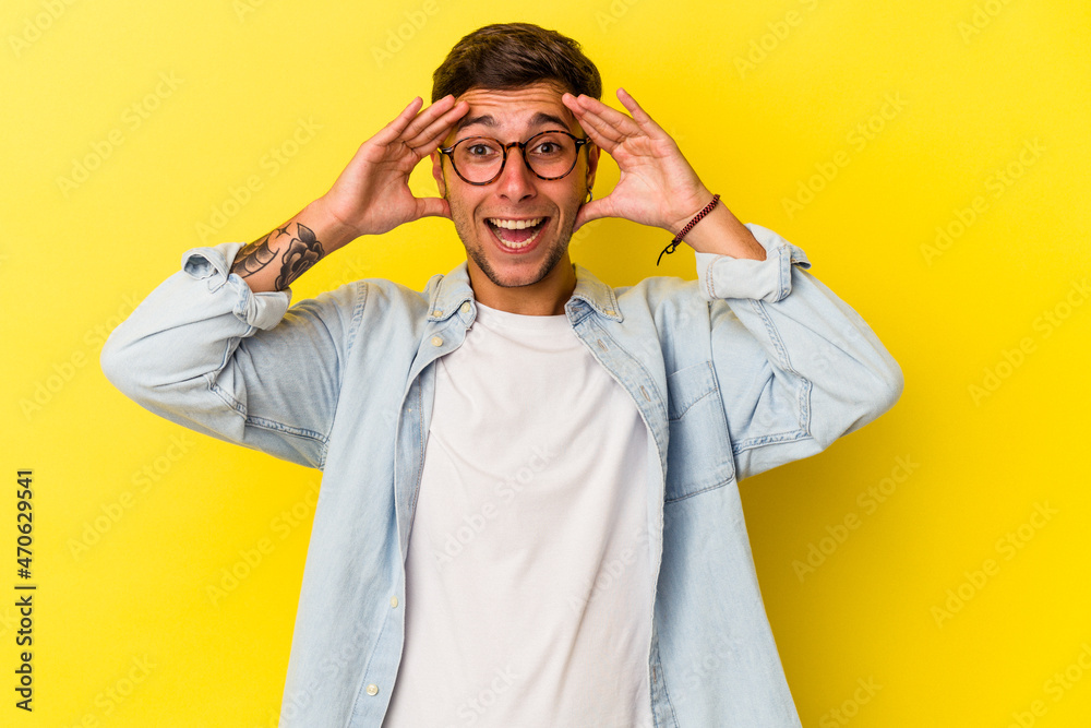 Young caucasian man with tattoos isolated on yellow background receiving a pleasant surprise, excited and raising hands. Young caucasian man with tattoos isolated on yellow background receiving a pleasant surprise, excited and raising hands.