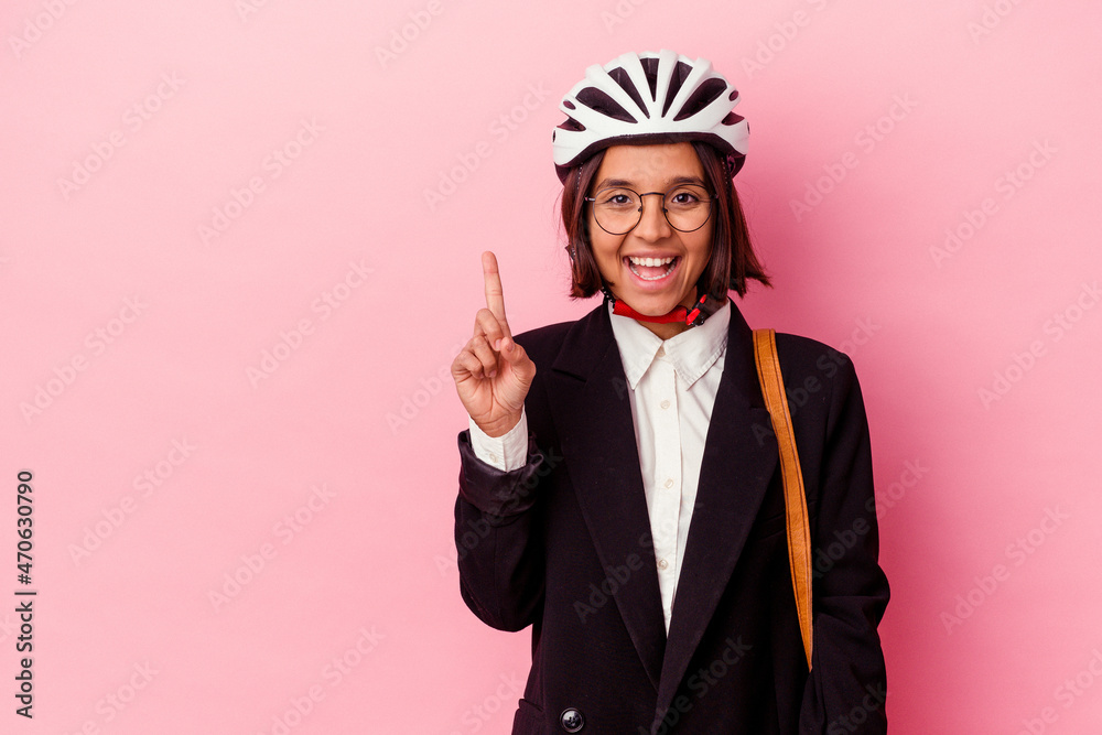 Young business mixed race woman wearing a bike helmet isolated on pink background showing number one with finger.