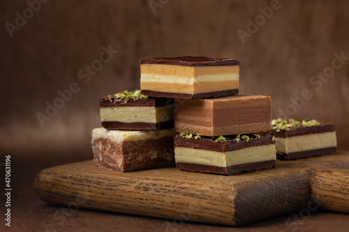 Italian cremino - chocolate typical shape is a cube, originally from Piedmont, composed by different layers, made with gianduja chocolate, coffee, pistacchio or hazelnut paste. On brown background.