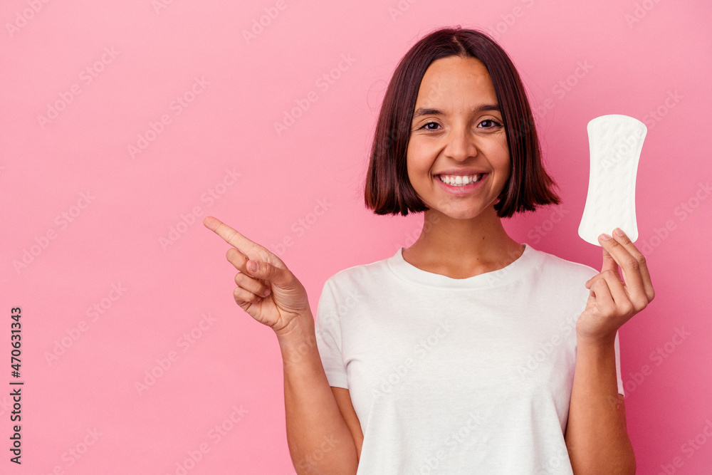 Young mixed race woman holding a compress isolated on pink background smiling and pointing aside, showing something at blank space. Young mixed race woman holding a compress isolated on pink background smiling and pointing aside, showing something at blank space.