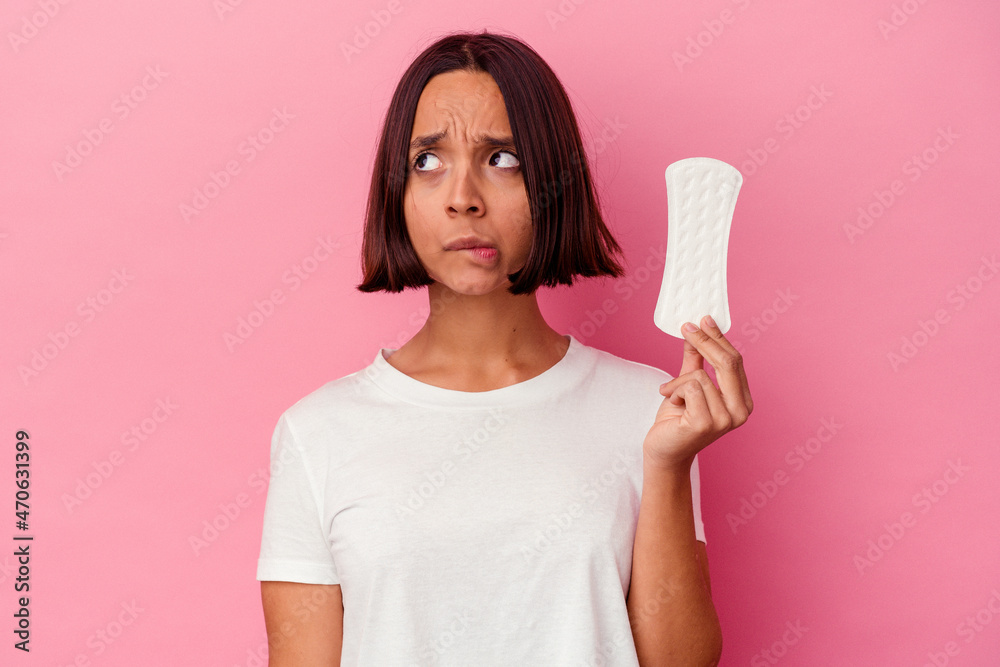 Young mixed race woman holding a compress isolated on pink background confused, feels doubtful and unsure. Young mixed race woman holding a compress isolated on pink background confused, feels doubtful and unsure.