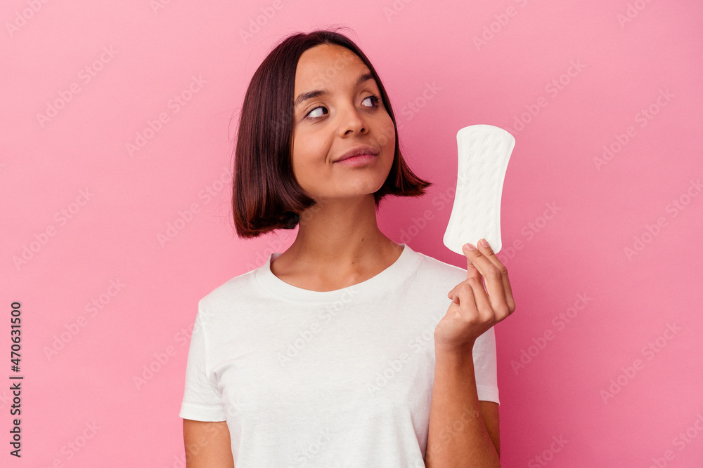 Young mixed race woman holding a compress isolated on pink background looks aside smiling, cheerful and pleasant. Young mixed race woman holding a compress isolated on pink background looks aside smiling, cheerful and pleasant.
