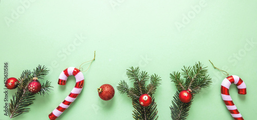 Christmas decoration border on pastel green background. Fresh fir twig, red balls and candy canes