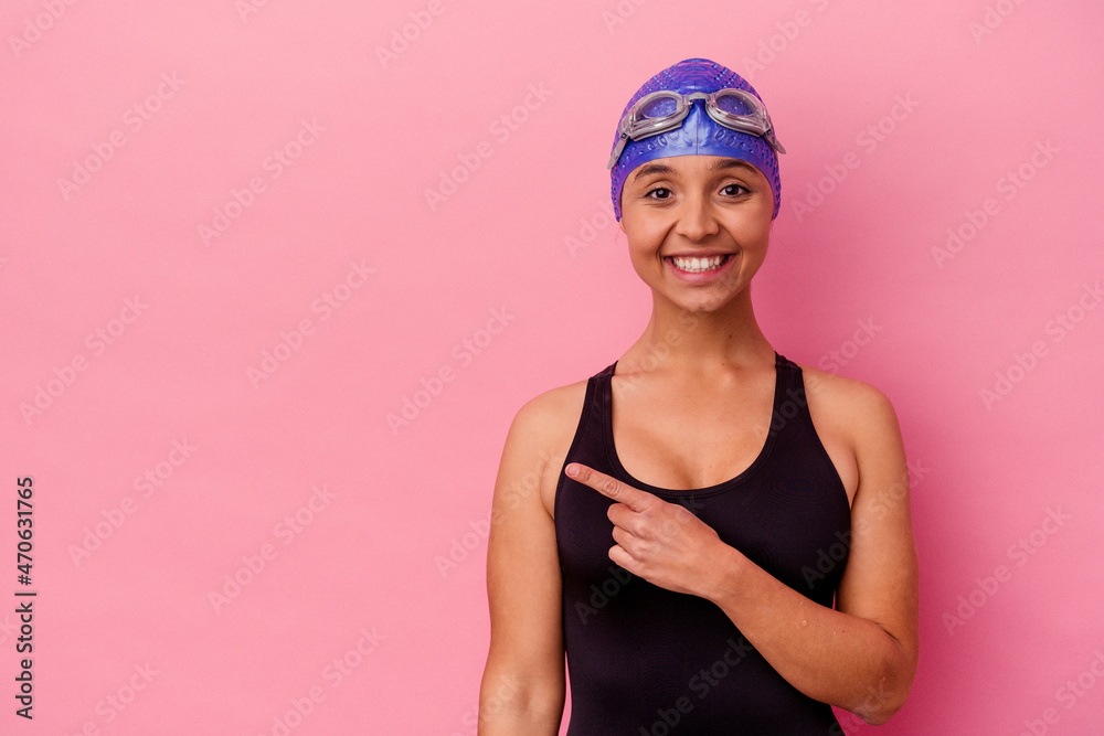 Young swimmer mixed race woman isolated on pink background smiling and pointing aside, showing something at blank space. Young swimmer mixed race woman isolated on pink background smiling and pointing aside, showing something at blank space.