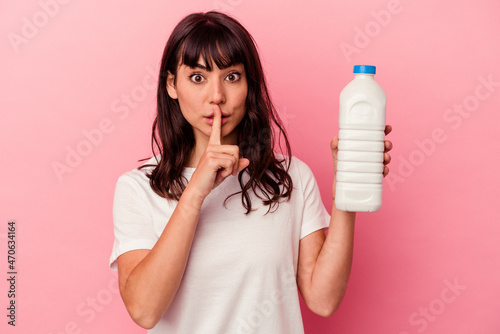 Young caucasian woman holding a bottle of milk isolated on pink background keeping a secret or asking for silence.