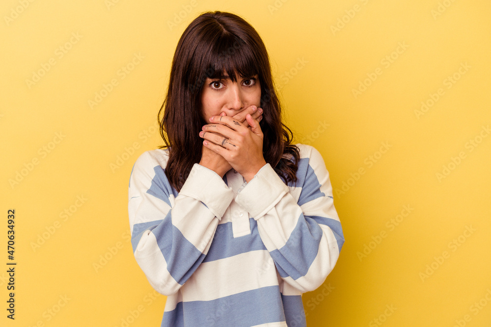 Young caucasian woman isolated on yellow background covering mouth with hands looking worried.