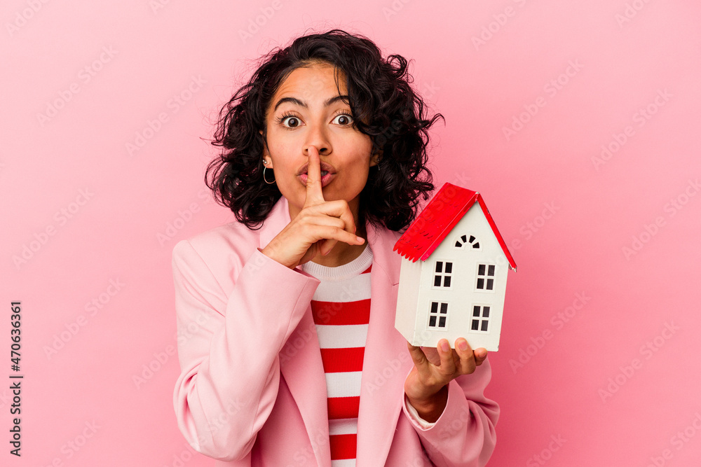 Φωτογραφία Young latin woman holding a toy house isolated on pink background keeping a secret or asking for silence