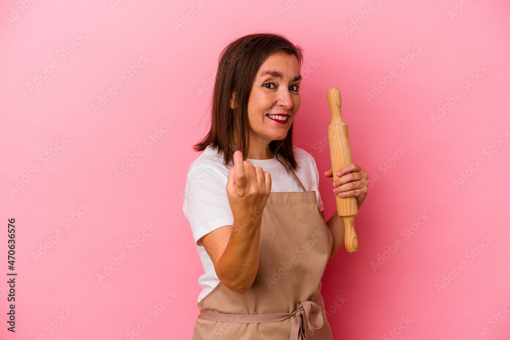 Middle age pastry chef woman isolated on pink background pointing with finger at you as if inviting come closer. Middle age pastry chef woman isolated on pink background pointing with finger at you as if inviting come closer.